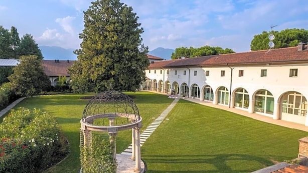 A courtyard with a gazebo, a large tree, and a building with arched windows. - Villa I Pini (Civitella in Val di Chiana)