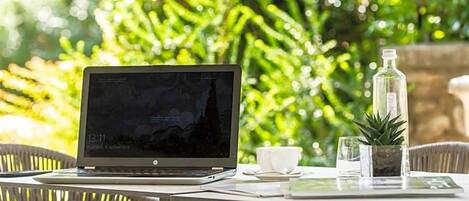 A laptop on a table with a cup and a small plant.