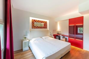 A modern hotel room with a large bed, a desk, and a red accent wall. - Villa I Pini (Civitella in Val di Chiana)