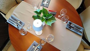 A round dining table with a white tablecloth, set with cutlery, glasses, and a potted plant.