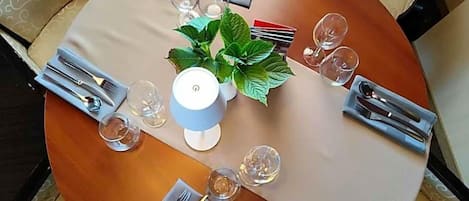 A round dining table with a white tablecloth, set with cutlery, glasses, and a potted plant.