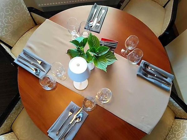 A round dining table with a white tablecloth, set with cutlery, glasses, and a potted plant. - Aviator (Pabianice)