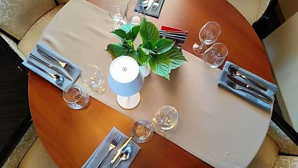 A round dining table with a white tablecloth, set with cutlery, glasses, and a potted plant. - Aviator (Pabianice)