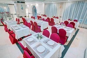 A banquet hall with multiple tables set for dining, red chairs, and a modern interior design. - Hayah Salam Silver Hotel (Madinah)