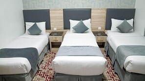 A hotel room with three single beds, a wooden headboard, and a patterned carpet. - Hayah Salam Silver Hotel (Madinah)