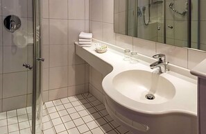 A modern bathroom with a glass shower enclosure, a white sink with a mirror, and neatly arranged toiletries. - Fischer S Hotel Brauhaus (Moessingen)