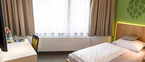 Habitación de hotel con cama, escritorio, silla, ventana con cortinas y pared con el logotipo de Hop.