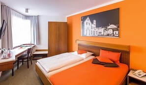 A hotel room with a bed, a desk, a chair, a wardrobe, and a painting on the wall. - Fischer S Hotel Brauhaus (Moessingen)