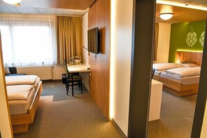 A hotel room with two beds, a desk, a chair, a television, and a mirror. - Fischer S Hotel Brauhaus (Moessingen)