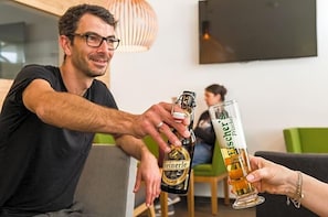 A person holding a bottle and a glass, likely containing beer, in a room with a green couch and a modern lamp. - Fischer S Hotel Brauhaus (Moessingen)