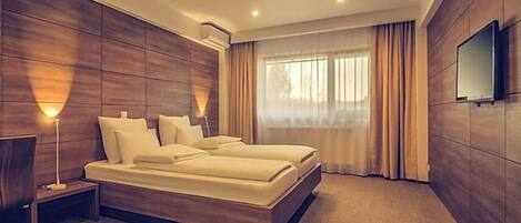 Habitación de hotel moderna con una cama grande, un televisor de pantalla plana y un ventanal con cortinas.