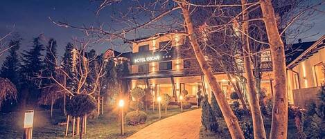 A hotel named 'HOTEL OSCAR' with a well-lit entrance, a paved pathway, and surrounding trees.