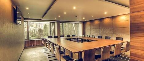 Un salón de conferencias con una larga mesa, sillas y ventanas amplias.