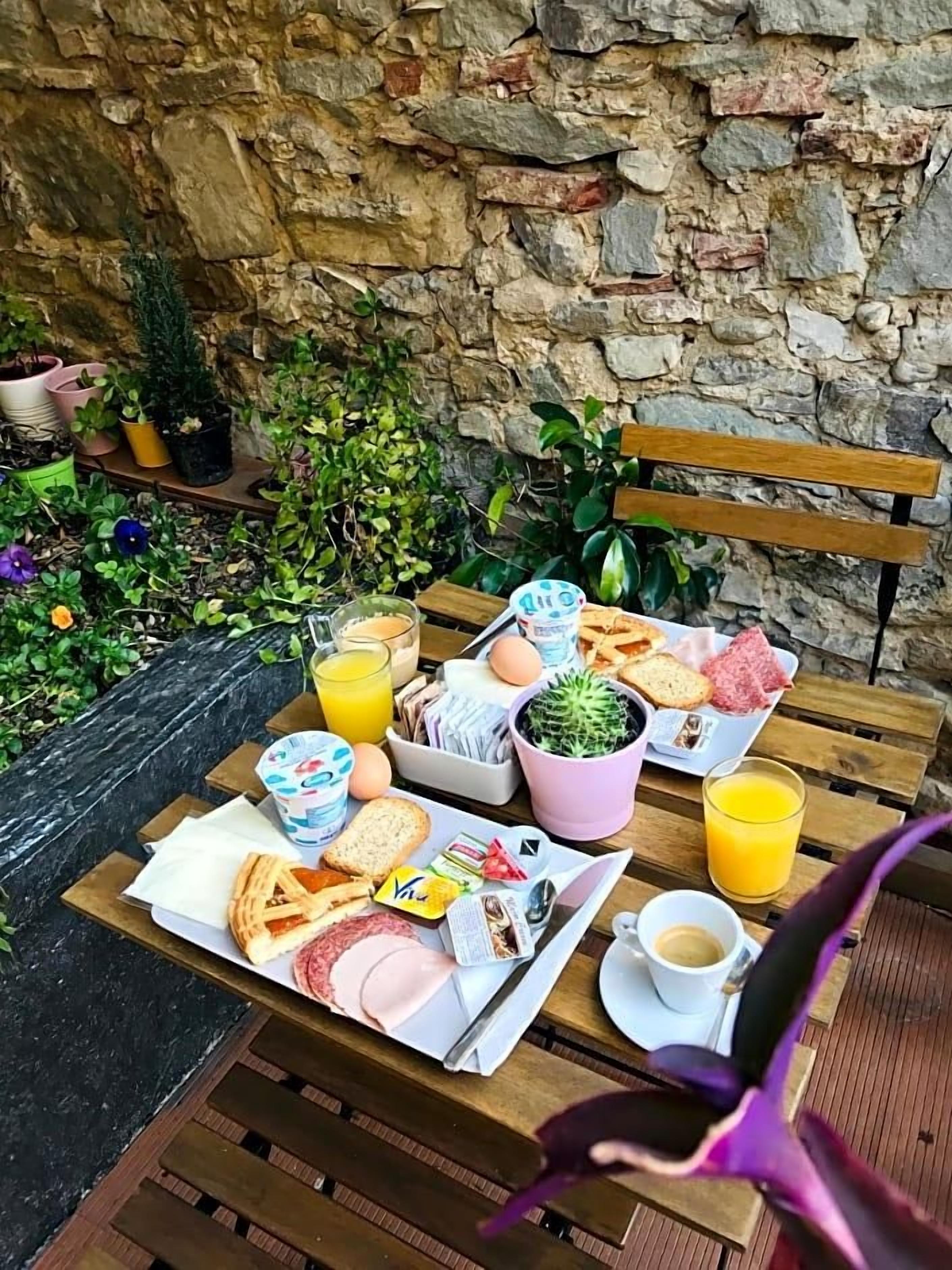 A breakfast setup on a wooden table with a stone wall background, including eggs, toast, bread, and juice.