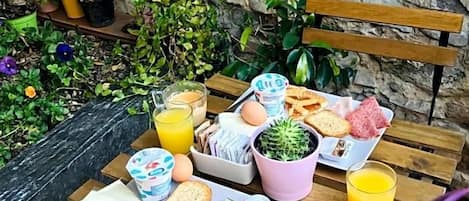 A breakfast setup on a wooden table with a stone wall background, including eggs, toast, bread, and juice.