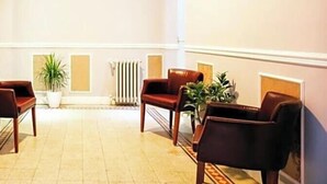 A hotel lobby with a high ceiling, a radiator, potted plants, and a painting of a building on the wall. - Hotel Aida (Florence)