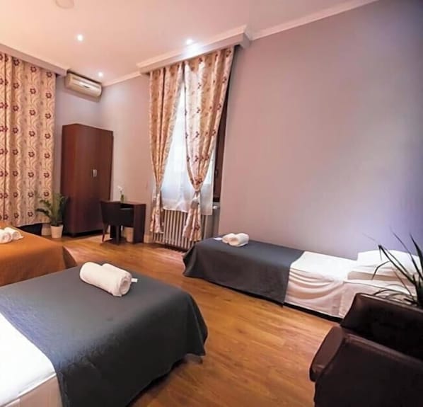 Ein Hotelzimmer mit zwei Betten, einem Schreibtisch, einem Kleiderschrank und einer Zimmerpflanze.