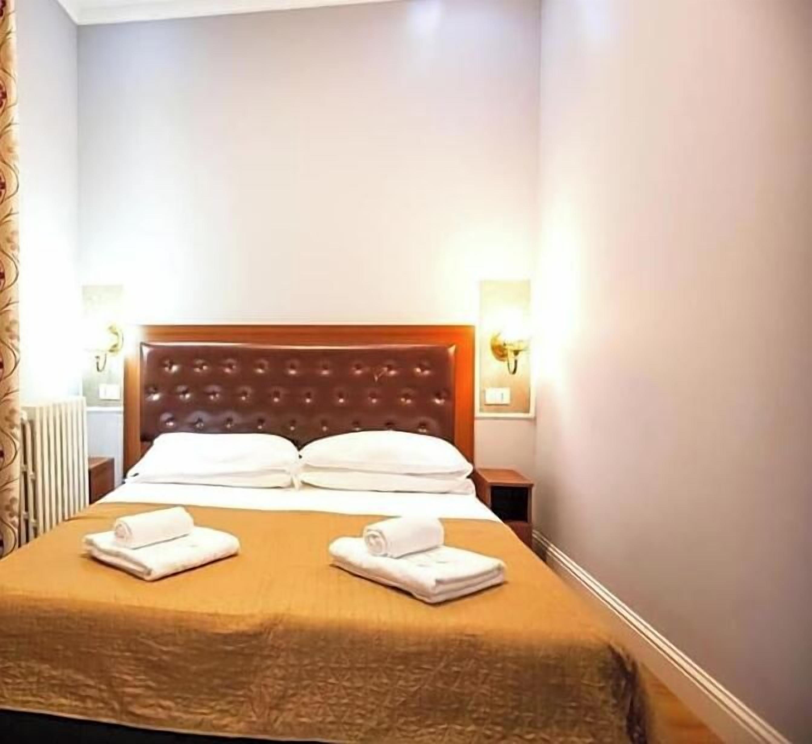 A hotel room with a large bed, two bedside tables, and a wall-mounted light fixture.