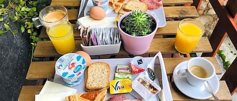 Bandeja de desayuno con huevos, pan, jamón, una planta y jugo, sobre una mesa de madera.