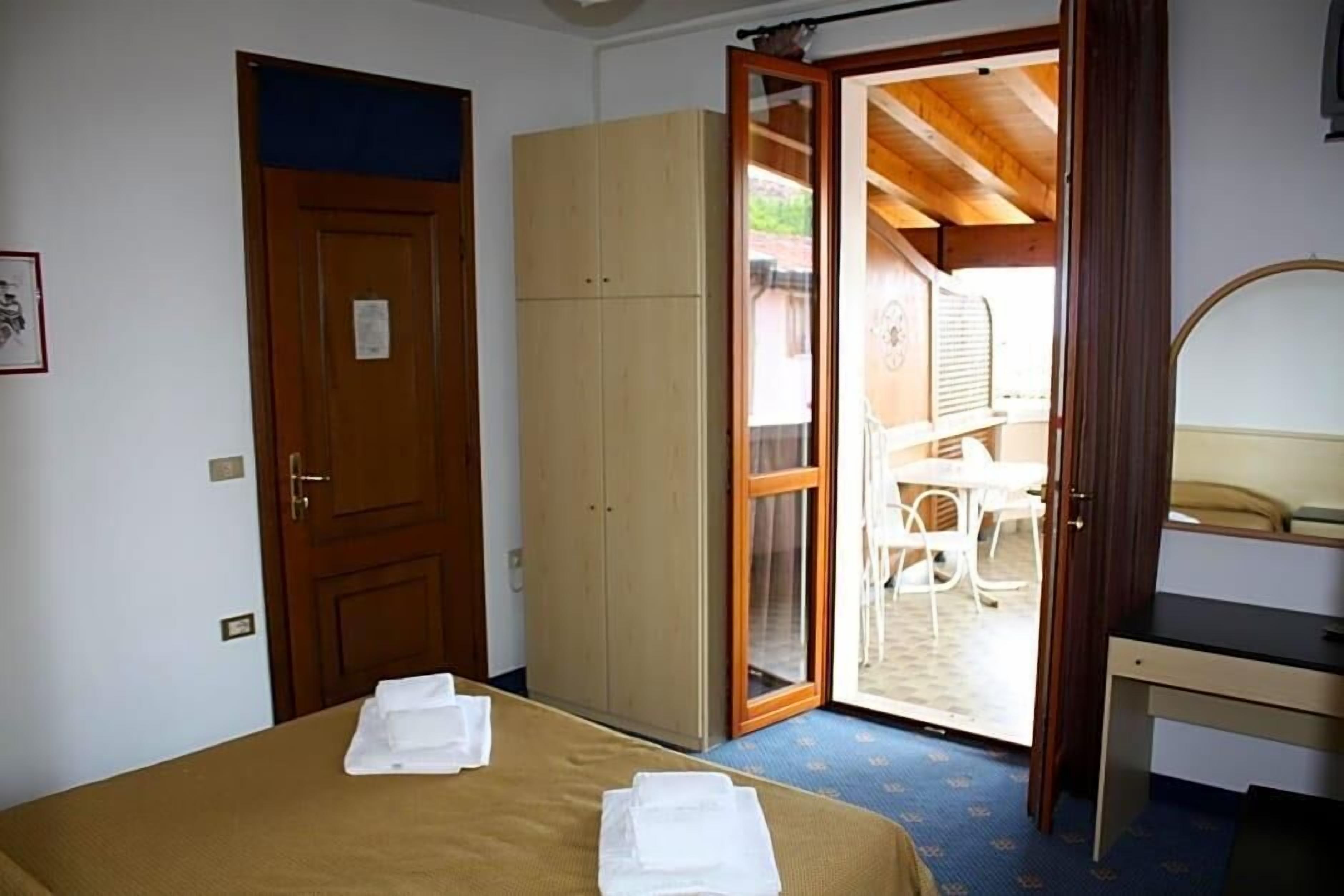 Un dormitorio con cama, armario, escritorio y puerta que da a un espacio exterior con mesa y sillas.