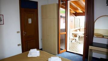 Un dormitorio con cama, armario, escritorio y puerta que da a un espacio exterior con mesa y sillas.