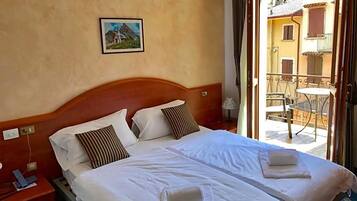 Ein Doppelbett mit zwei Kissen, ein Nachttisch mit Telefon und ein Blick auf einen Außenbalkon mit Tisch und Stühlen.