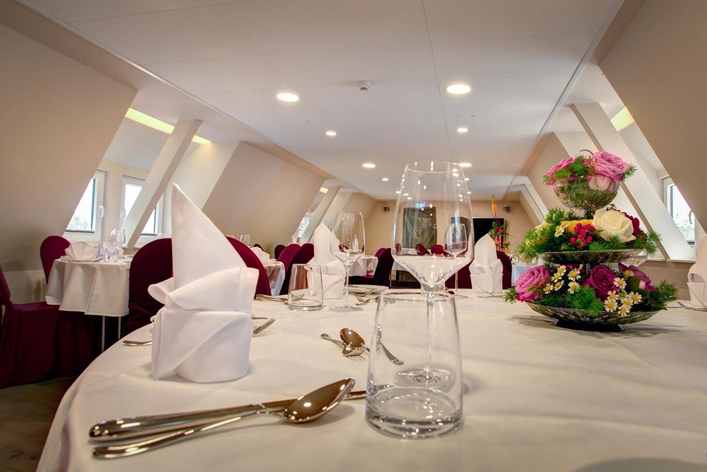 Un espace repas avec des tables mises pour le repas, comprenant couverts et verrerie, ainsi qu’un arrangement floral décoratif.
