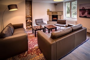 A modern living room with leather sofas, a fireplace, a coffee table, and a large window with a view of greenery. - Weserhotel Schwager (Holzminden)