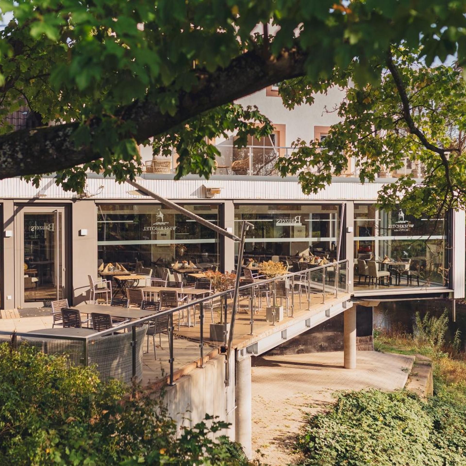 Een modern gebouw met een glazen gevel, een terras en een brug die verschillende niveaus met elkaar verbindt.
