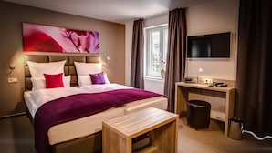 Ein Hotelzimmer mit Bett, Schreibtisch, Fernseher und einem Fenster mit Vorhängen.