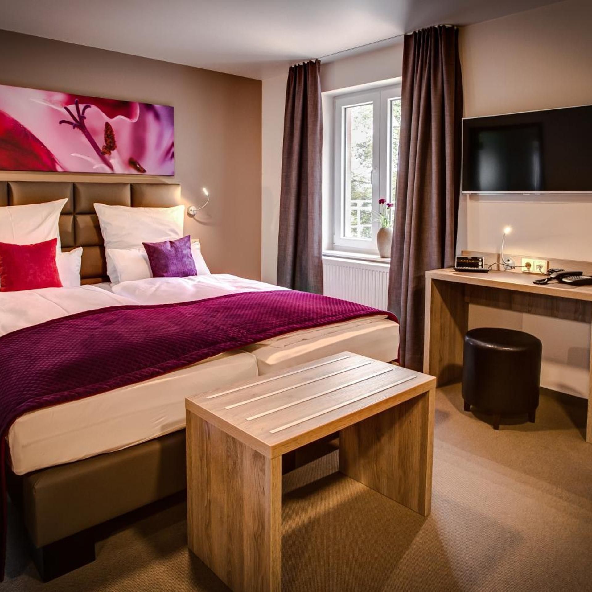 Een hotelkamer met een bed, een bureau, een televisie en een raam met gordijnen.