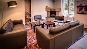 Ein modernes Wohnzimmer mit Ledersofas, einem Kamin, einem Couchtisch und einem großen Fenster mit Blick ins Grüne.