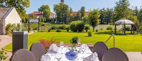 A table set for dining outdoors with a view of a church steeple and a garden.