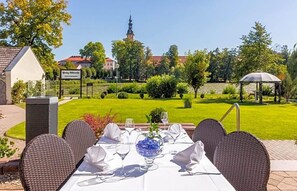 A table set for dining outdoors with a view of a church steeple and a garden. - Hotel Prinz Albrecht (Neuzelle)