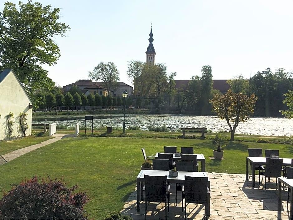 Un espacio al aire libre con mesas y sillas, un río y una torre de iglesia a lo lejos.