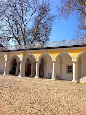 A courtyard with a cobblestone floor, white columns, and a yellow building with arched doorways. - Hotel Prinz Albrecht (Neuzelle)