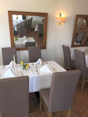 Un coin repas avec une table dressée pour quatre personnes, des chaises, un miroir et un luminaire fixé au mur.