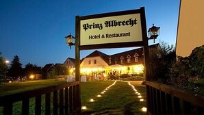 A hotel entrance with a sign reading 'Prinz Mbrecht Hotel & Restaurant,' a pathway leading to the building, and a well-lit lawn area. - Hotel Prinz Albrecht (Neuzelle)