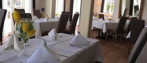 Comedor con mesas dispuestas para el servicio, sillas y un gran ventanal que proporciona luz natural.