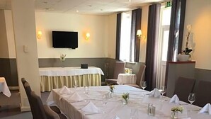 A conference room with long tables set for dining, a television mounted on the wall, and a window with curtains. - Hotel Prinz Albrecht (Neuzelle)