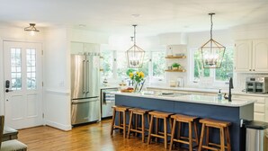 Una cocina moderna con una isla grande, taburetes de madera, electrodomésticos de acero inoxidable e iluminación colgante.