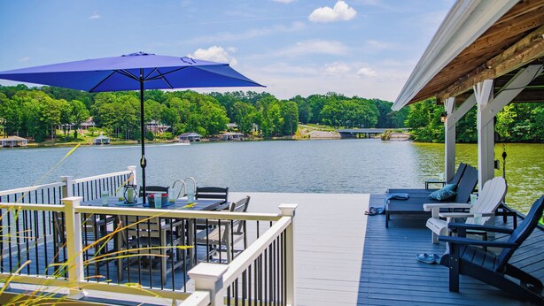 Una terraza con mobiliario exterior, un parasol grande y vistas a un lago y árboles.