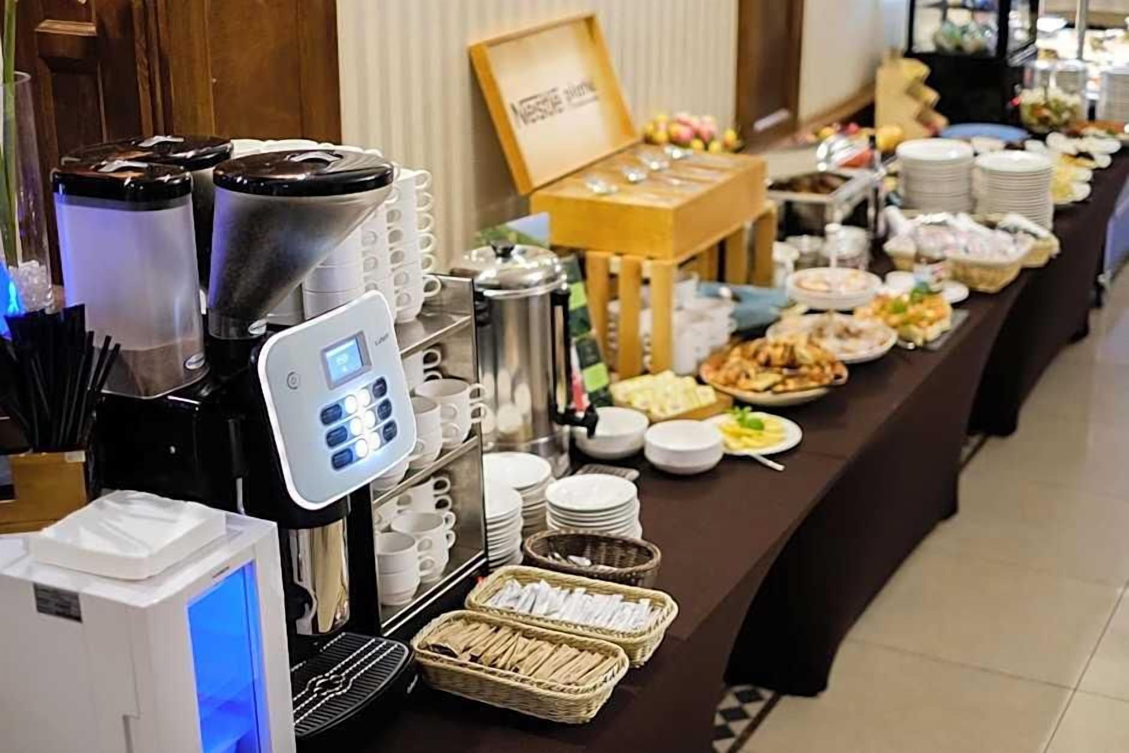 Disposição de buffet com máquinas de café, pratos, tigelas e utensílios.