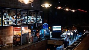Zona de bar con estantes llenos de botellas de licor, un monitor de computadora y equipo de bar.