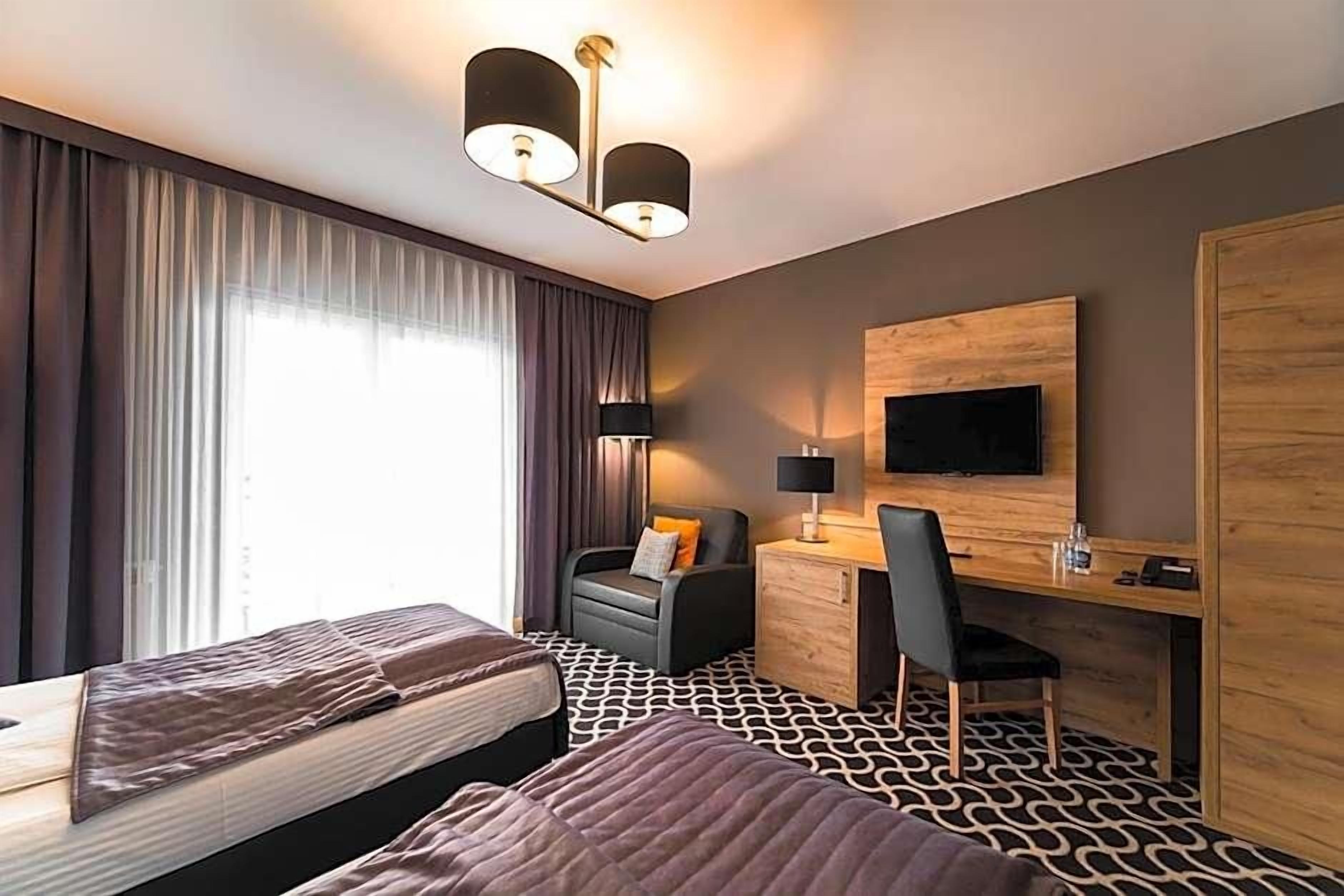 A hotel room with two beds, a desk, a chair, a TV, and a wardrobe.