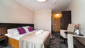 Una habitación de hotel con cama, escritorio, silla, lámpara y una puerta que da a otra habitación.