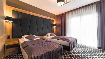 A hotel room with two beds, a large padded headboard, wall-mounted lights, and a patterned carpet.