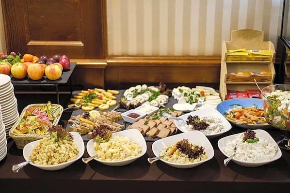 A buffet table with various food items and a fruit display. - Hotel Coloseum (Jaroslaw)