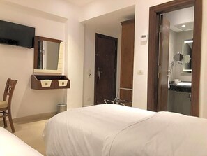 A hotel room with a bed, a chair, a TV, a mirror, a door, and a bathroom visible through an open door. - Maxim Hotel (Cairo)