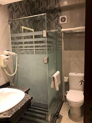 A bathroom with a glass-enclosed shower, a sink with a granite countertop, and a toilet. - Maxim Hotel (Cairo)